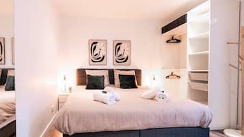 Un dormitorio moderno con una cama grande, dos obras de arte colgadas en la pared, una mesita de noche con lámpara y un armario empotrado con espacio para colgar ropa.