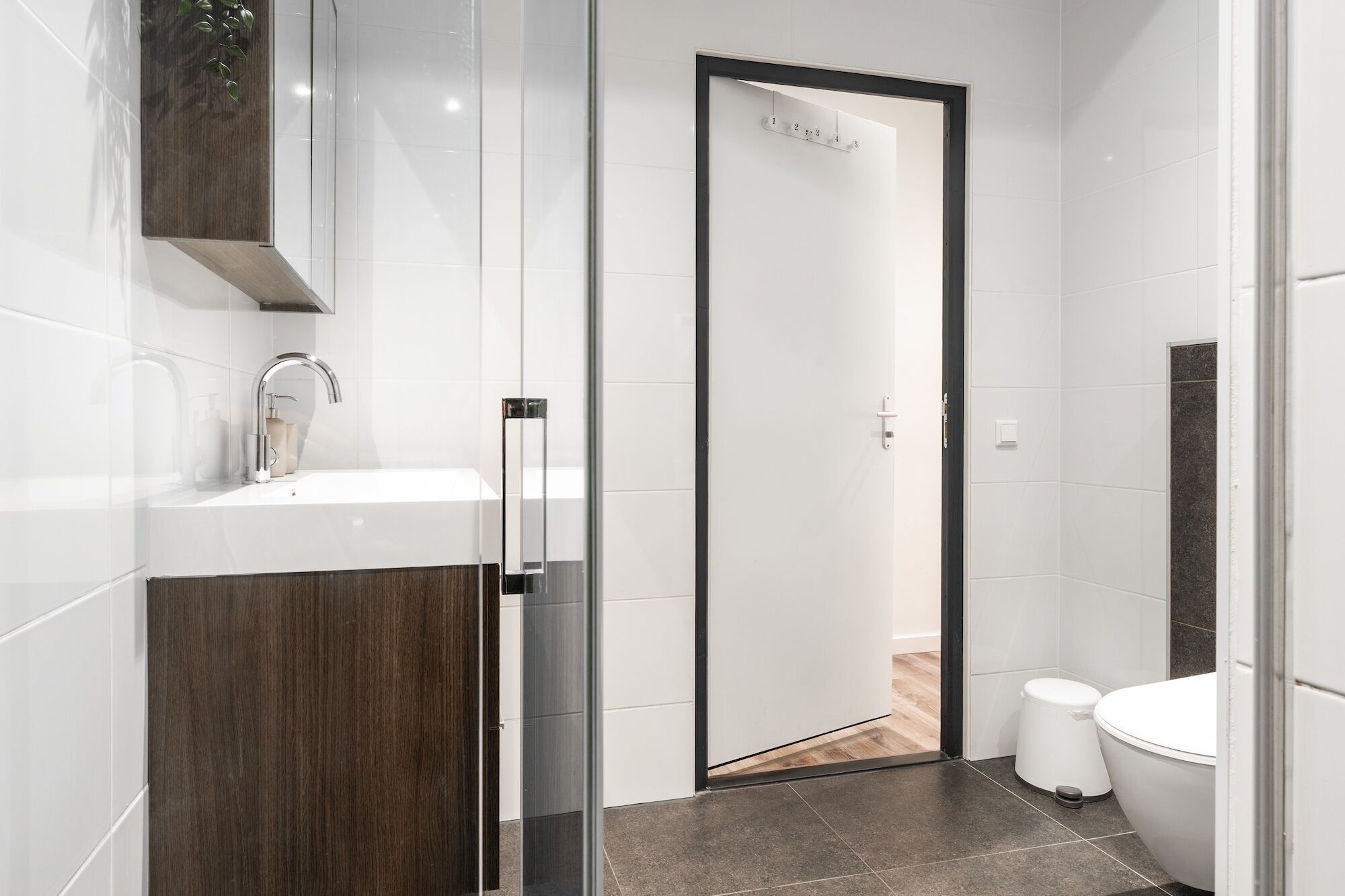 Un baño moderno con cabina de ducha de vidrio, un lavabo blanco con grifo cromado y un mueble de tocador de madera oscura.