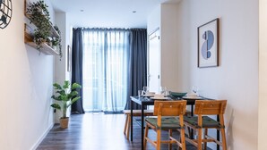 Un coin repas avec une table dressée pour quatre personnes, des chaises en bois, une plante en pot et une grande fenêtre avec des rideaux.