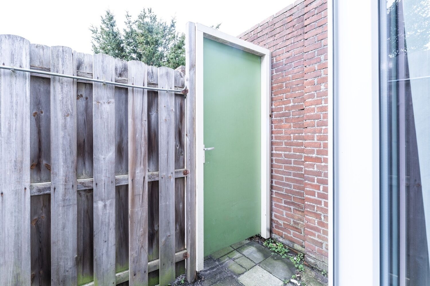 Una puerta verde junto a una valla de madera y un muro de ladrillo.