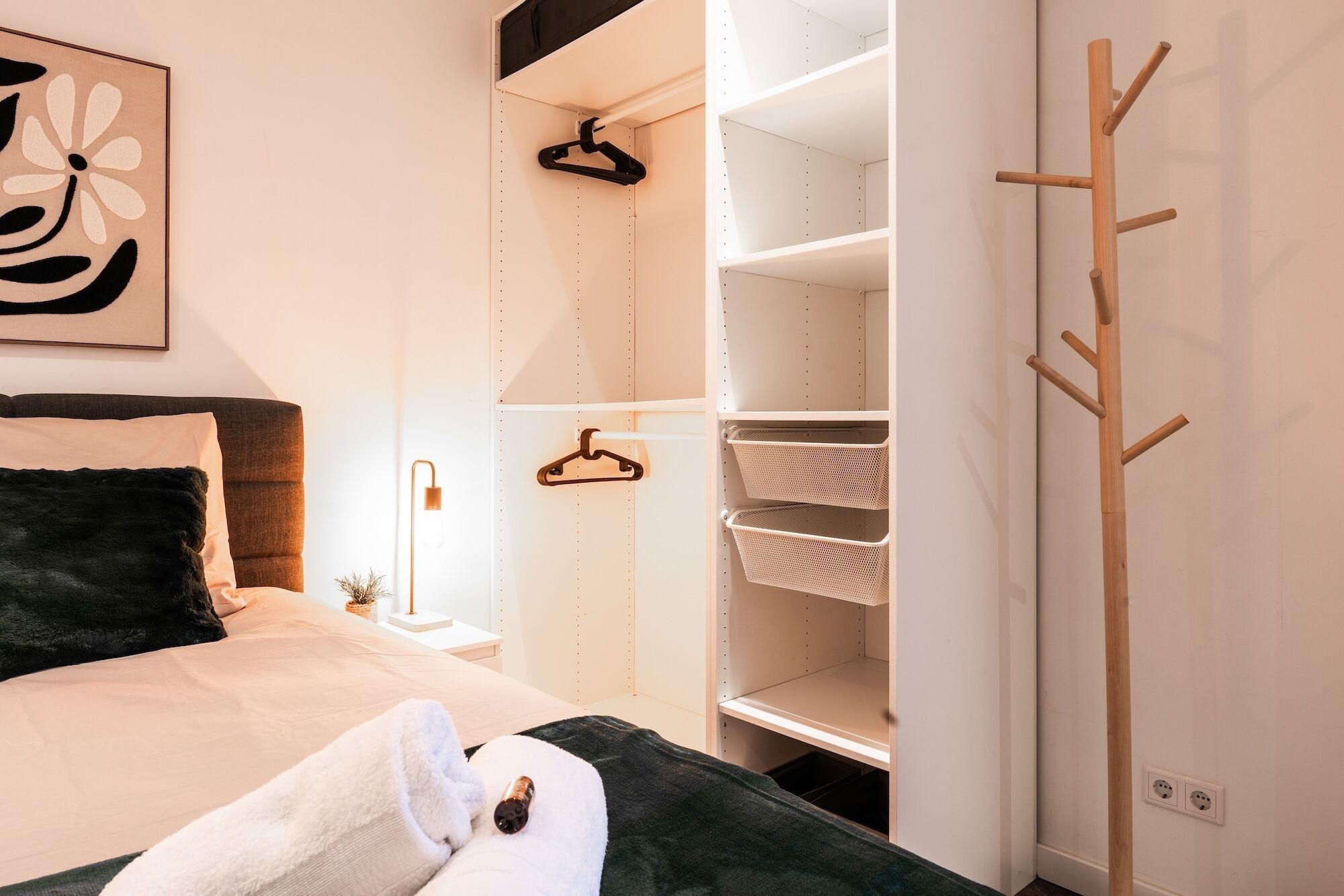 Une chambre à coucher comprenant un lit, une table de chevet, un porte-manteau mural et une armoire avec des étagères.