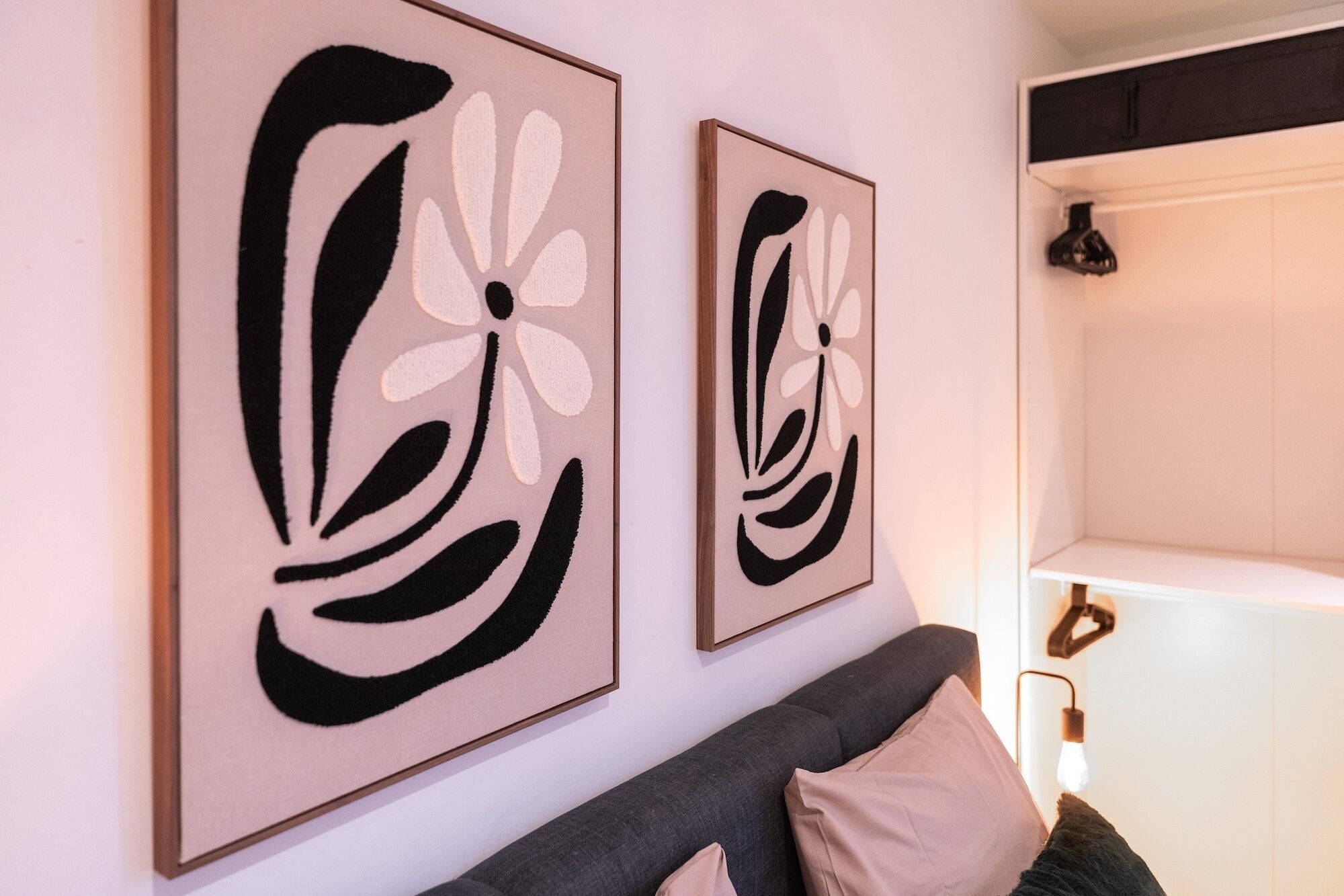 Dos cuadros abstractos en una pared, un sofá gris con cojines y un estante blanco.