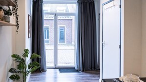 Une chambre d’hôtel moderne dotée d’une grande porte-fenêtre coulissante donnant sur une cour intérieure, d’un plancher en bois et d’un coin repas avec une table dressée pour deux personnes.