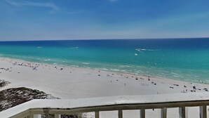 A beach with a clear sky, sandy shore, and a railing in the foreground.