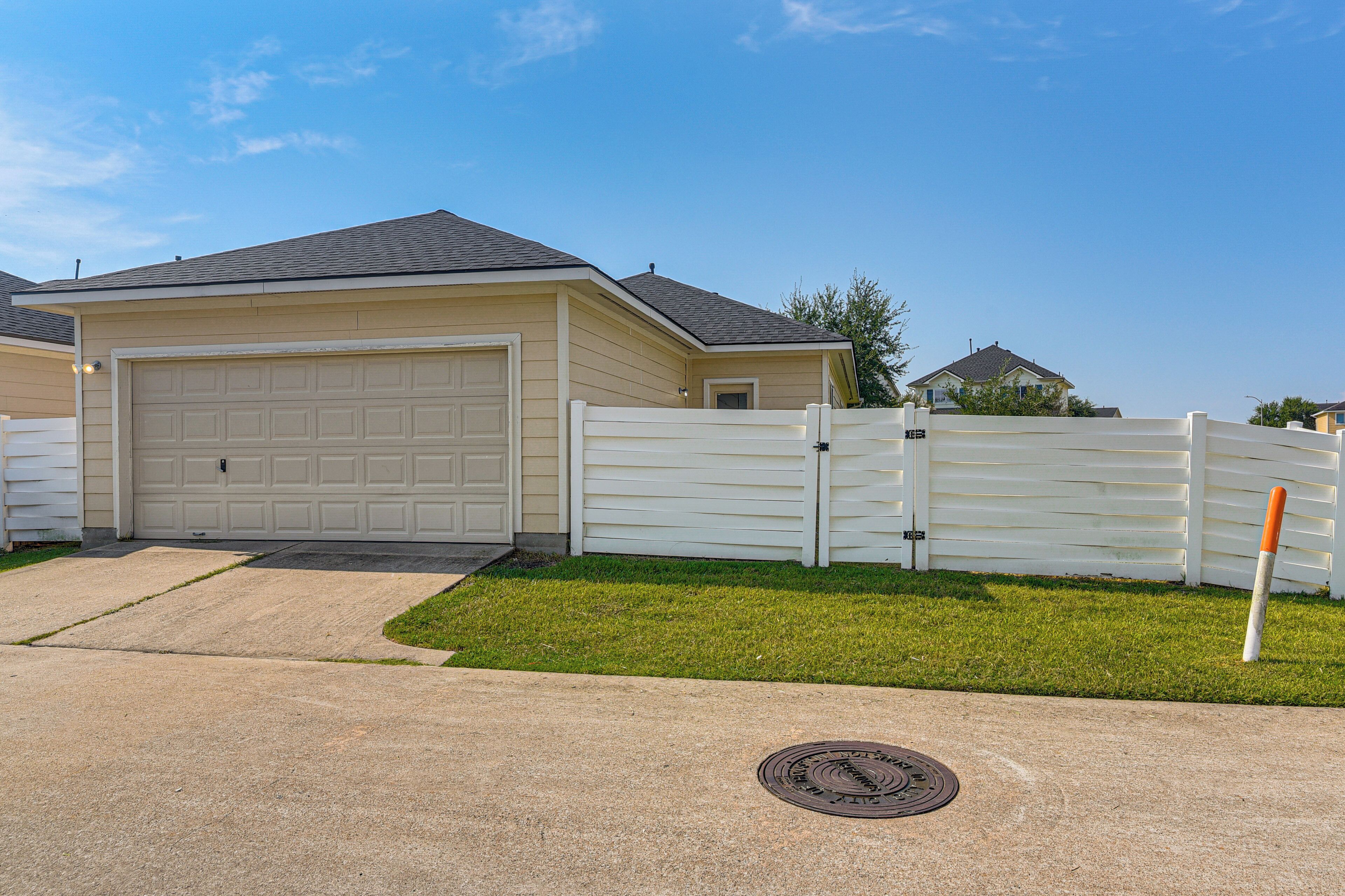 A single-story house with a garage, a white fence, and a grassy yard.