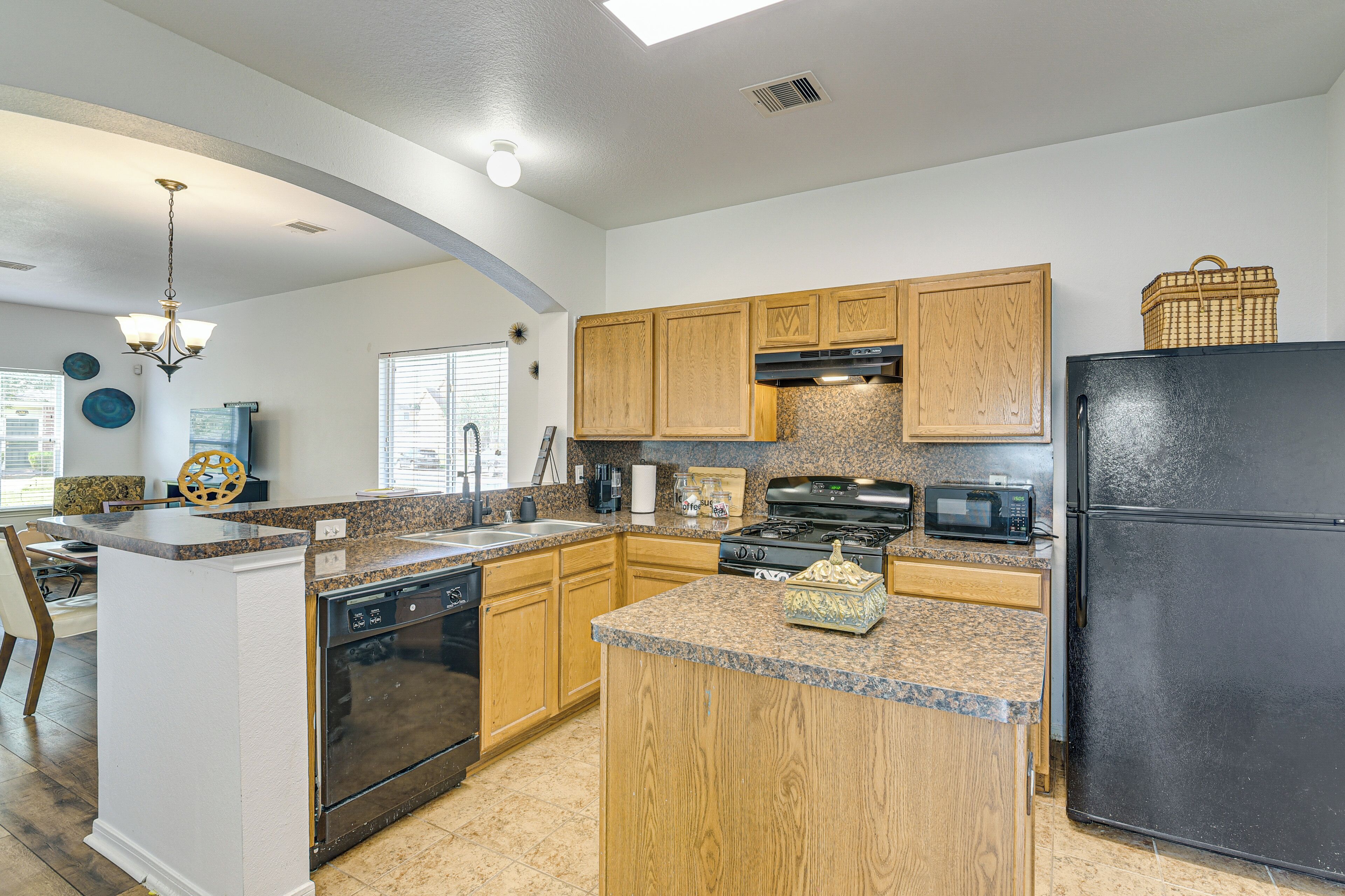 A modern kitchen with granite countertops, wooden cabinets, a black refrigerator, and a central island.