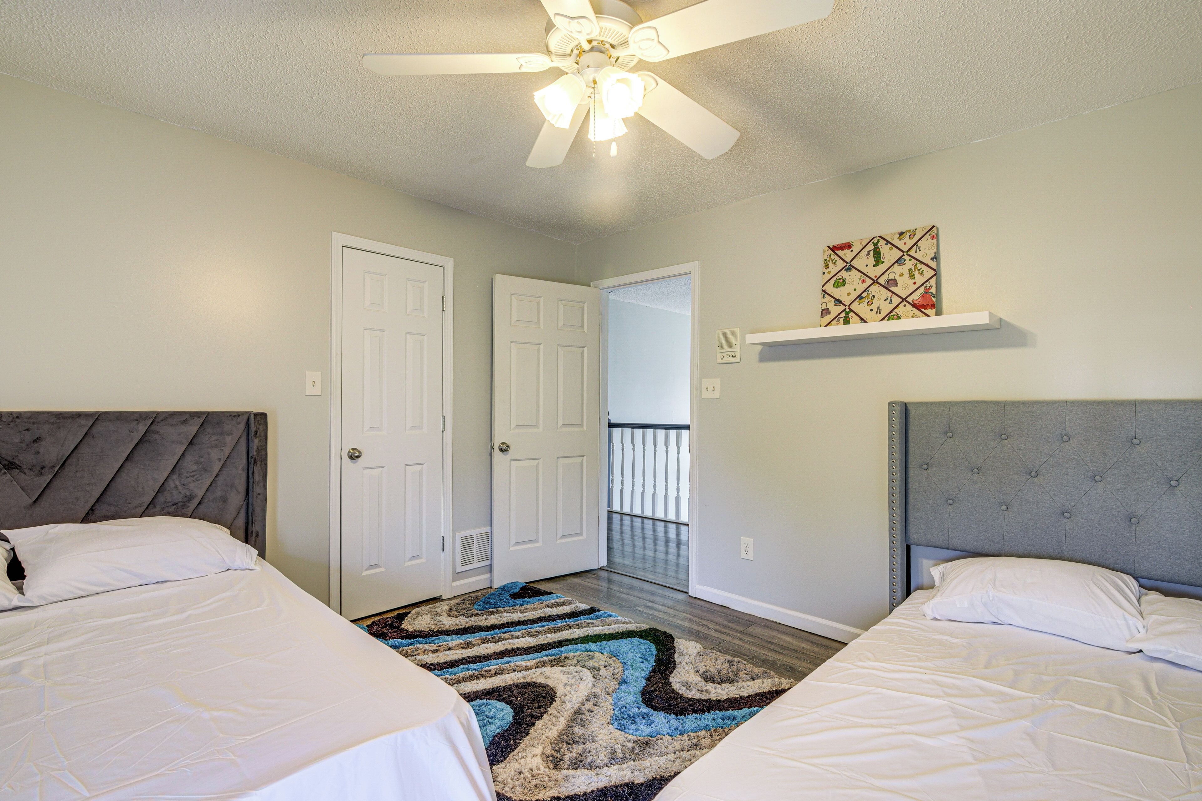 A bedroom with two beds, a ceiling fan, a door, and a small shelf with a decorative item.