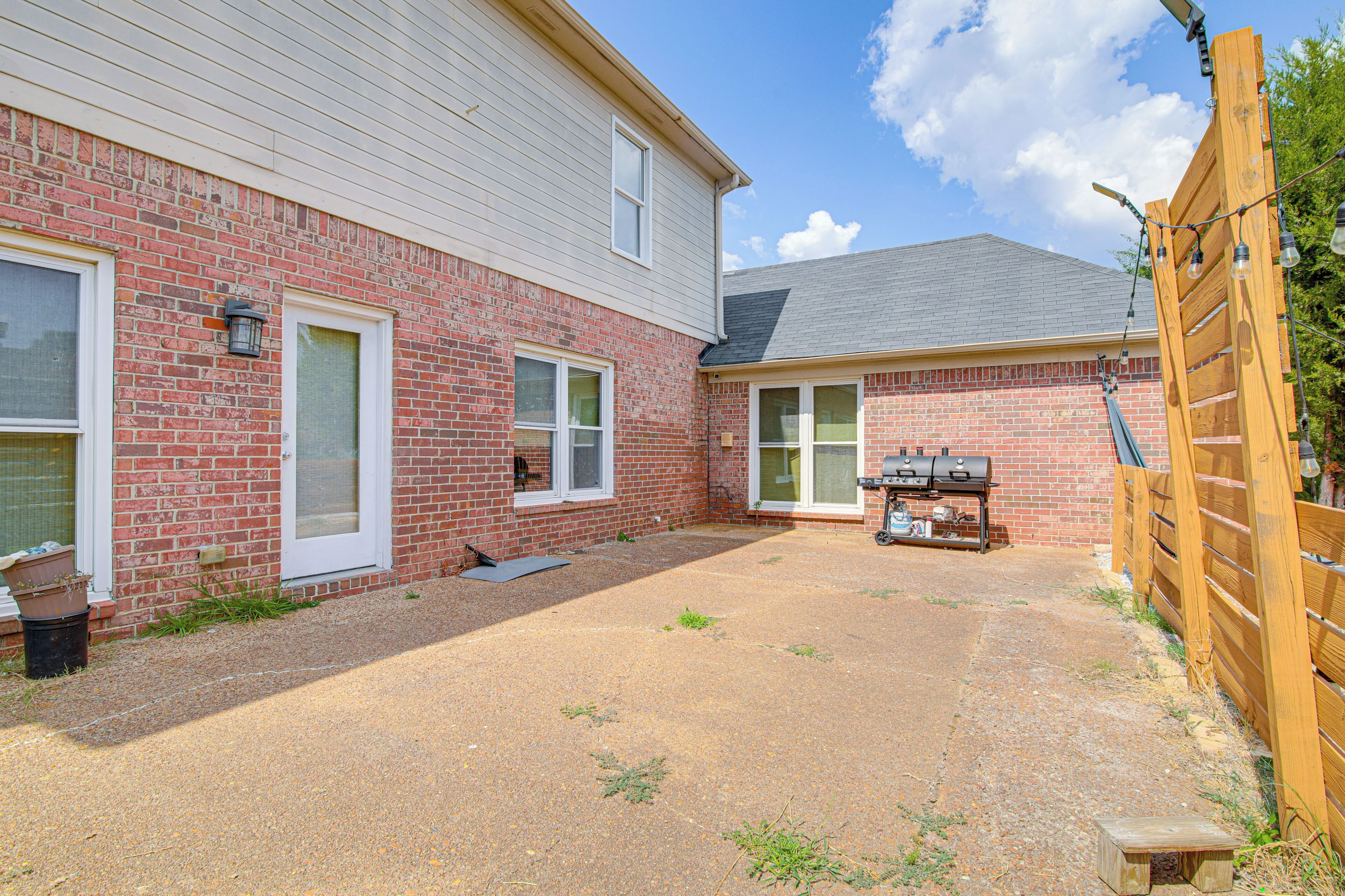 A two-story brick house with a covered patio, a barbecue grill, and a wooden fence.