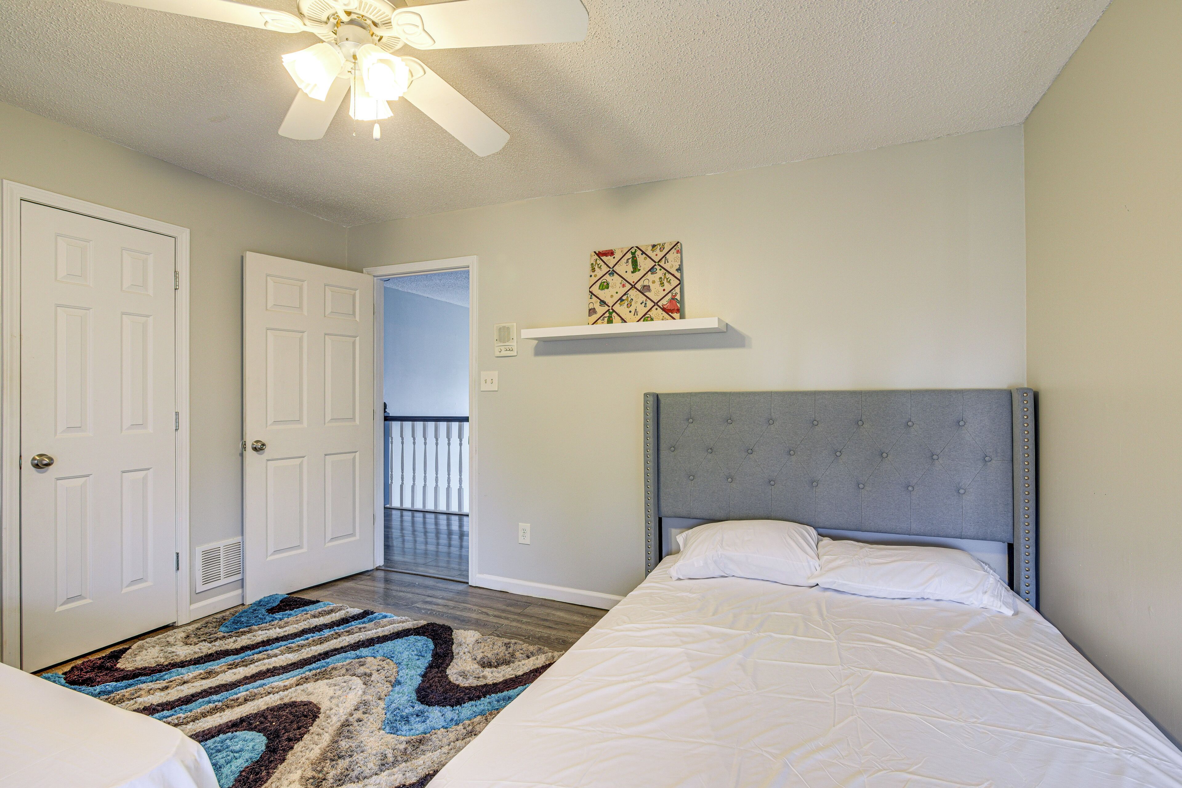 A bedroom with a bed, a ceiling fan, a door, a hallway, and a balcony.