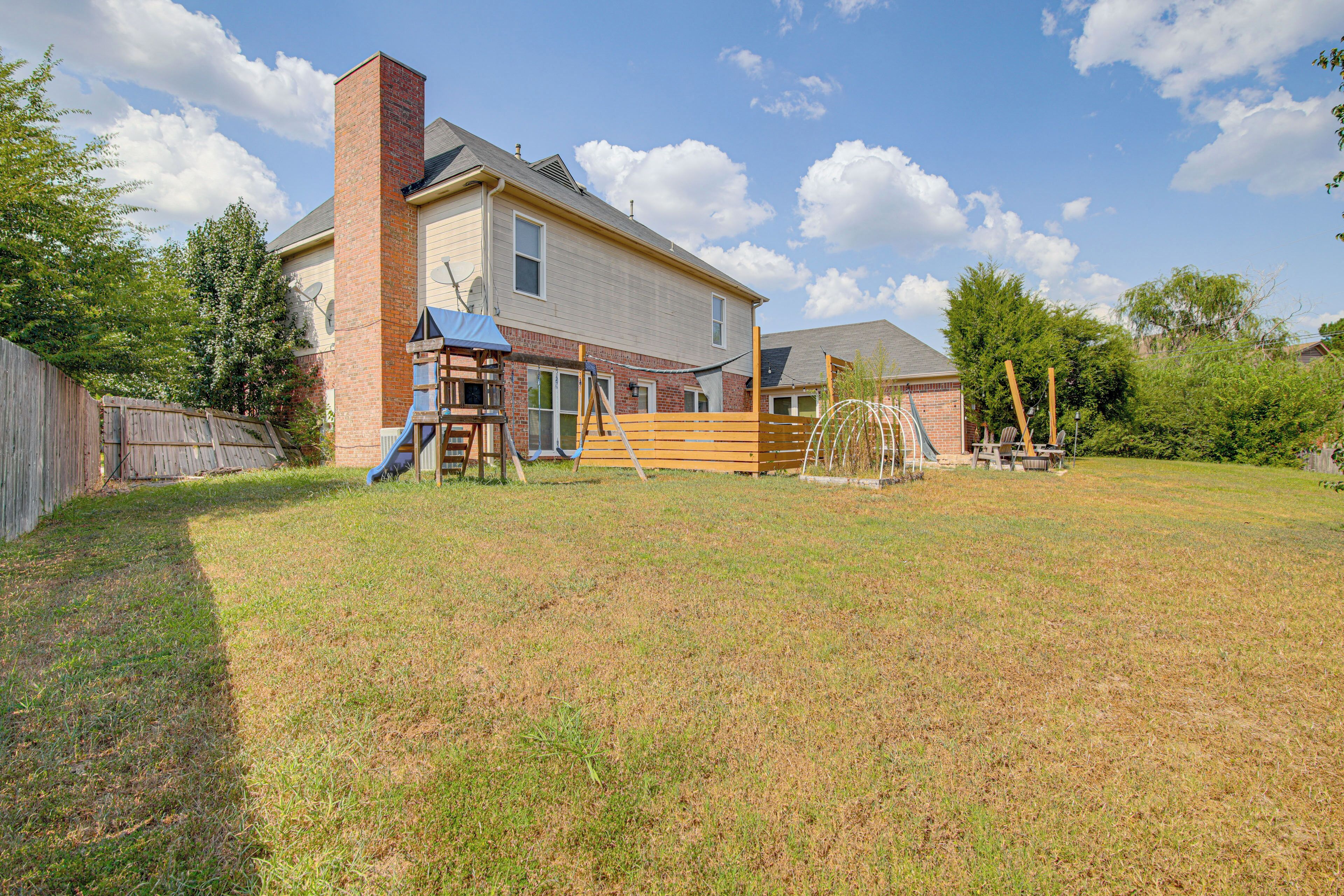 A two-story house with a brick chimney, a wooden deck, and a play structure in the yard.