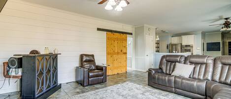 A living room with a leather sofa, a brown leather chair, a wooden door, and a ceiling fan.