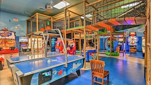 A multi-level indoor play area with various arcade games, a ping pong table, and a wooden chair.