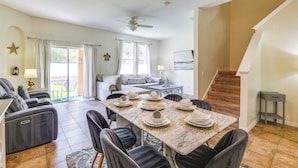 A spacious living area with a dining table set for six, a sofa, a ceiling fan, and a staircase leading to another level.