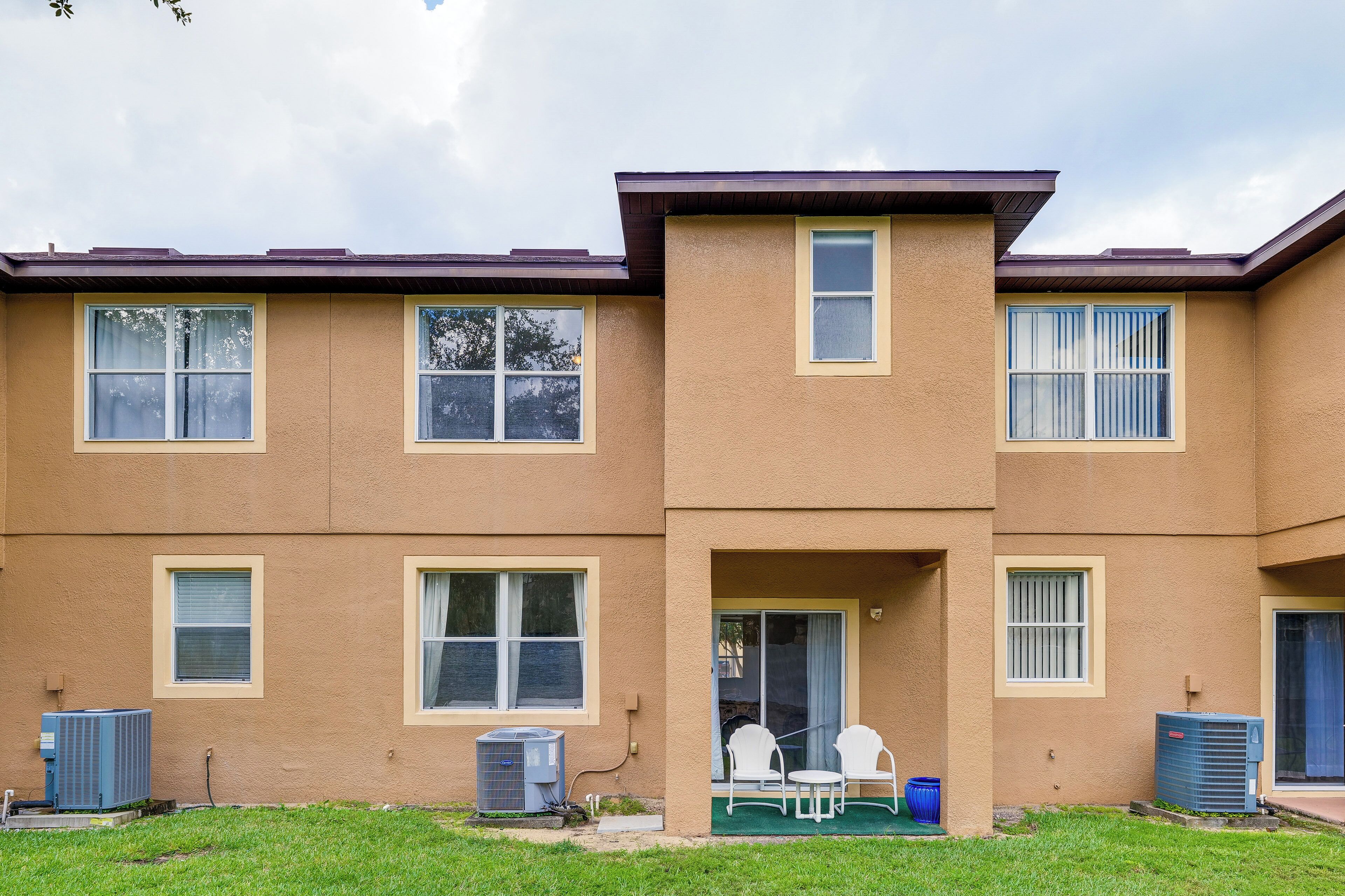 A two-story apartment building with a flat roof, multiple windows, and a small outdoor seating area with chairs.
