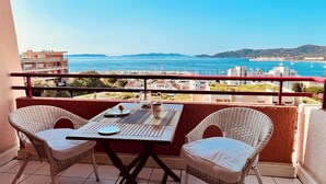 A balcony with wicker chairs and a table, overlooking a coastal view with buildings and boats. - Magnificent Grand STUDIO 28m2+ CLIM + sea view Terrace180- / south 8m2/+Box (Asc) (Le Lavandou)