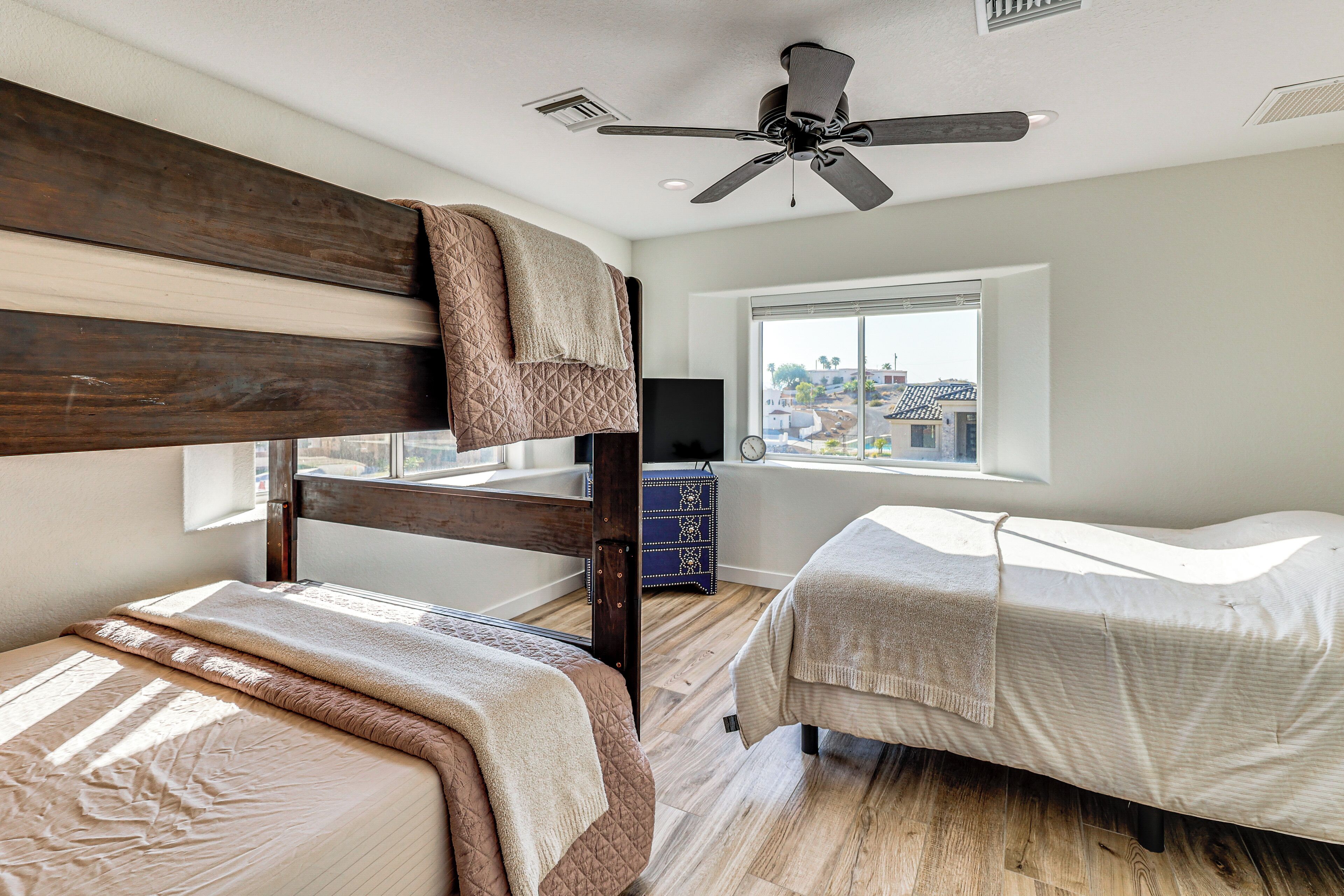 Une chambre avec un lit superposé, un lit simple, un ventilateur de plafond, une fenêtre avec vue et une petite table sur laquelle se trouve un téléviseur.