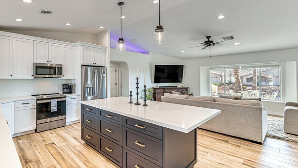 A modern kitchen with white cabinets, a central island, and a dining area with a sofa and TV. - Fully Furnished Poolside Oasis 5 Mi to Lake Havasu (Lake Havasu City)