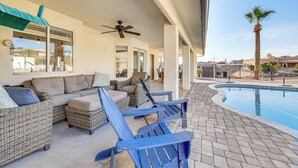 A poolside area with wicker furniture, a ceiling fan, and a view of a palm tree and buildings in the background. - Fully Furnished Poolside Oasis 5 Mi to Lake Havasu (Lake Havasu City)