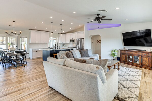A spacious living room with a large sofa, a dining area with a table and chairs, and a kitchen area with white cabinets and appliances. - Fully Furnished Poolside Oasis 5 Mi to Lake Havasu (Lake Havasu City)