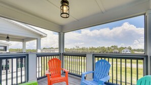 Un porche cubierto con vista a la playa, con tres sillas Adirondack en rojo, azul y verde.