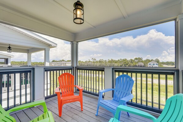 A covered porch with a view of the beach, featuring three Adirondack chairs in red, blue, and green.