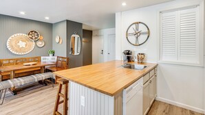 Une cuisine moderne dotée d’un îlot central en bois, de meubles blancs et d’un lave-vaisselle encastré.