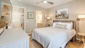 Une chambre à coucher avec un lit, un ventilateur de plafond, une table de chevet, une lampe et un tableau au mur.