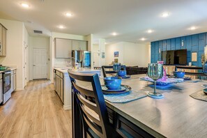 A modern kitchen with wooden flooring, a dining area with blue tableware, and a large TV on the wall. - Spacious Home Near Dtwn Psl: Travel Nurses Welcome (Port Saint Lucie)