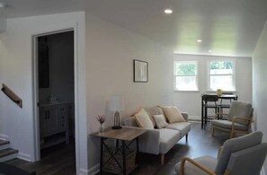 A spacious living area with a sofa, chairs, a small table, and a kitchen area in the background. - Sarah's Place, Grove City (Grove City)