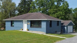 Una casa a un piano con tetto scuro, rivestimento azzurro chiaro, una porta d'ingresso e un garage.