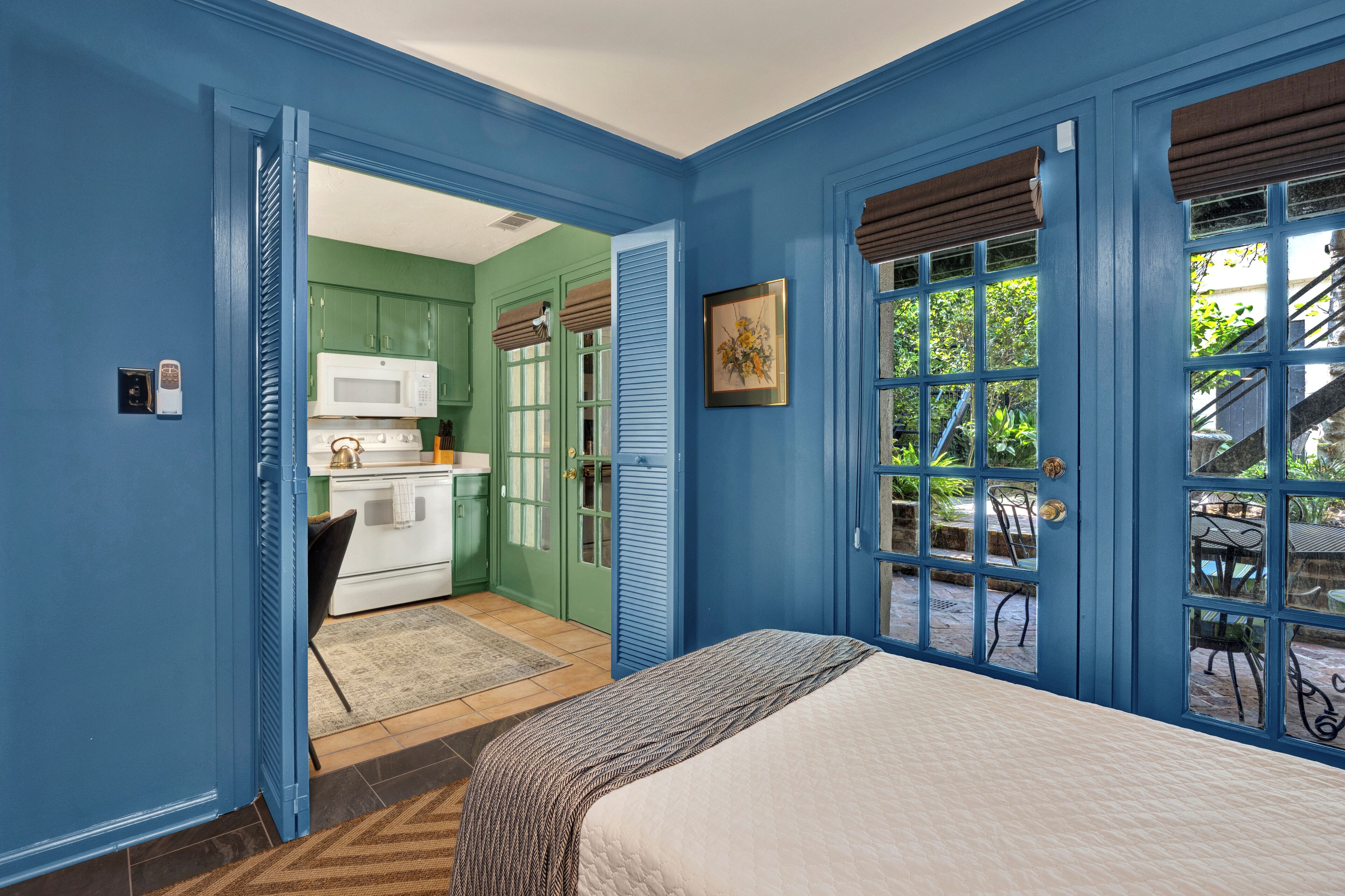 Un dormitorio con cama, vista a la cocina y puerta que da a un espacio exterior.