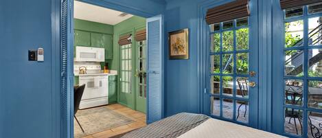 Un dormitorio con cama, vista a la cocina y puerta que da a un espacio exterior.