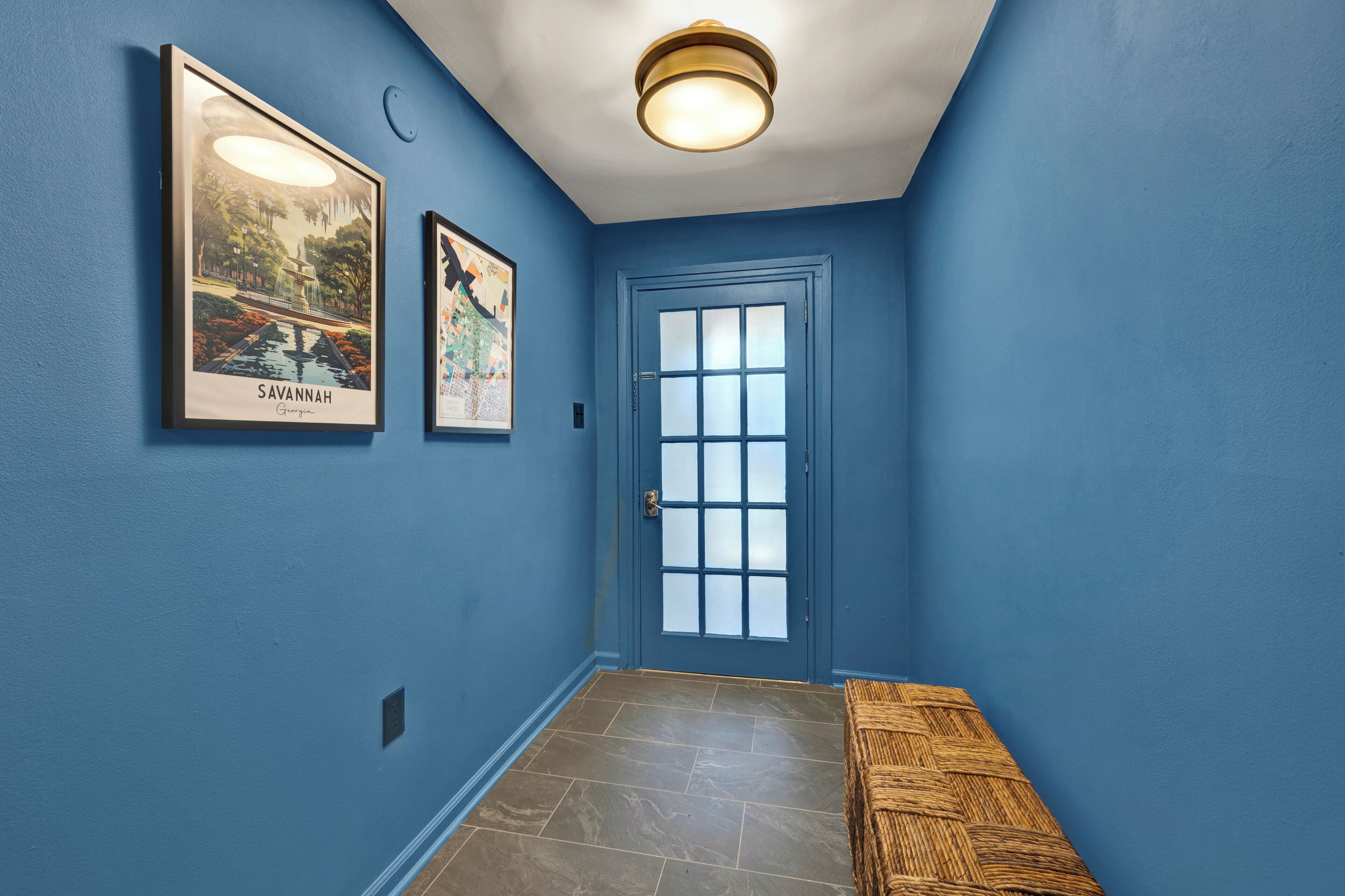 A hallway with blue walls, a door with frosted glass panels, and two framed pictures on the wall.