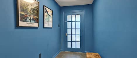 A hallway with blue walls, a door with frosted glass panels, and two framed pictures on the wall.