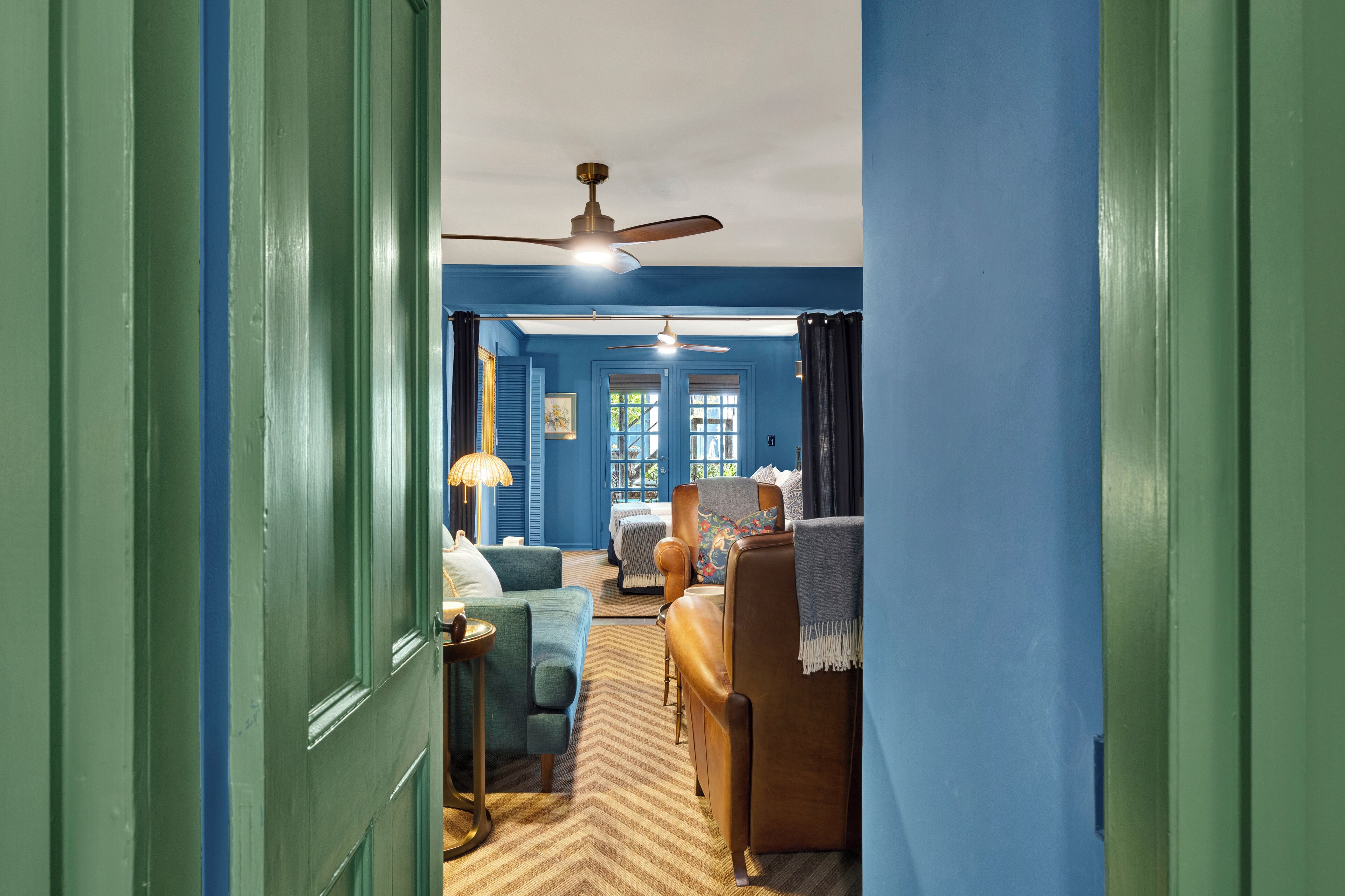 A hallway leading to a bedroom with a ceiling fan, a bed, a chair, and a lamp.
