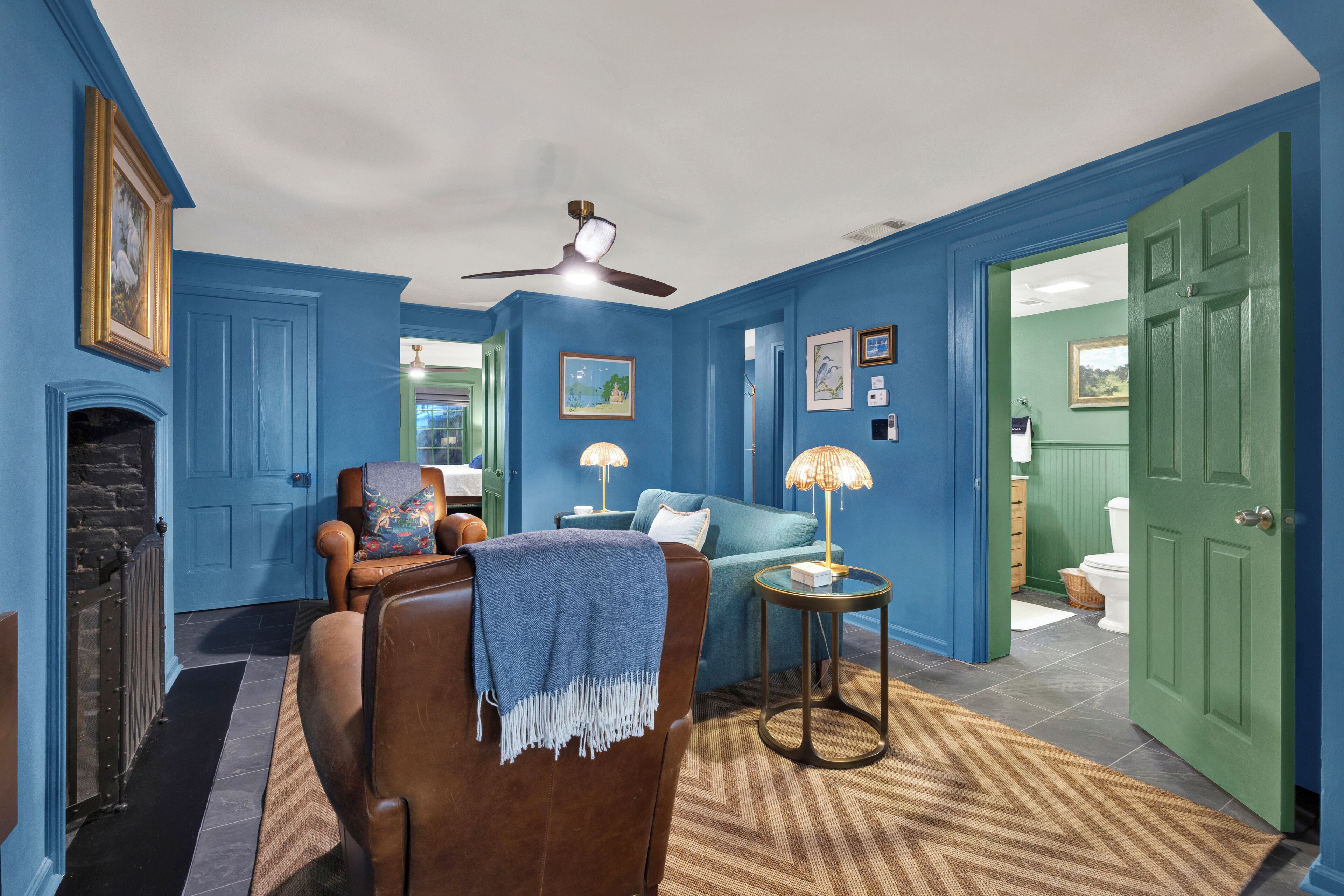 A room with blue walls, a brown leather chair, a blue sofa, a fireplace, and a ceiling fan.