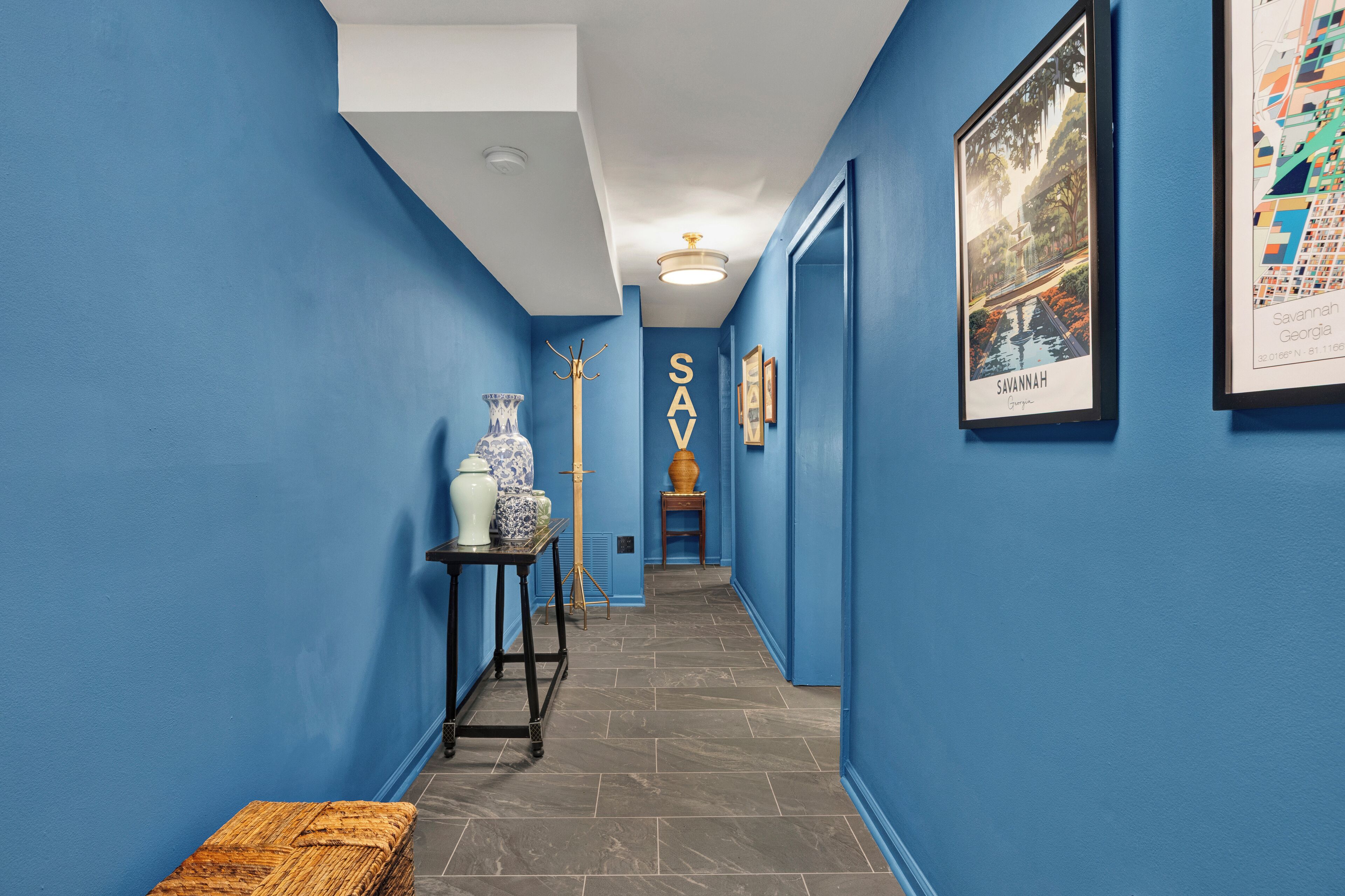A hallway with blue walls, a framed map, and a decorative vase.