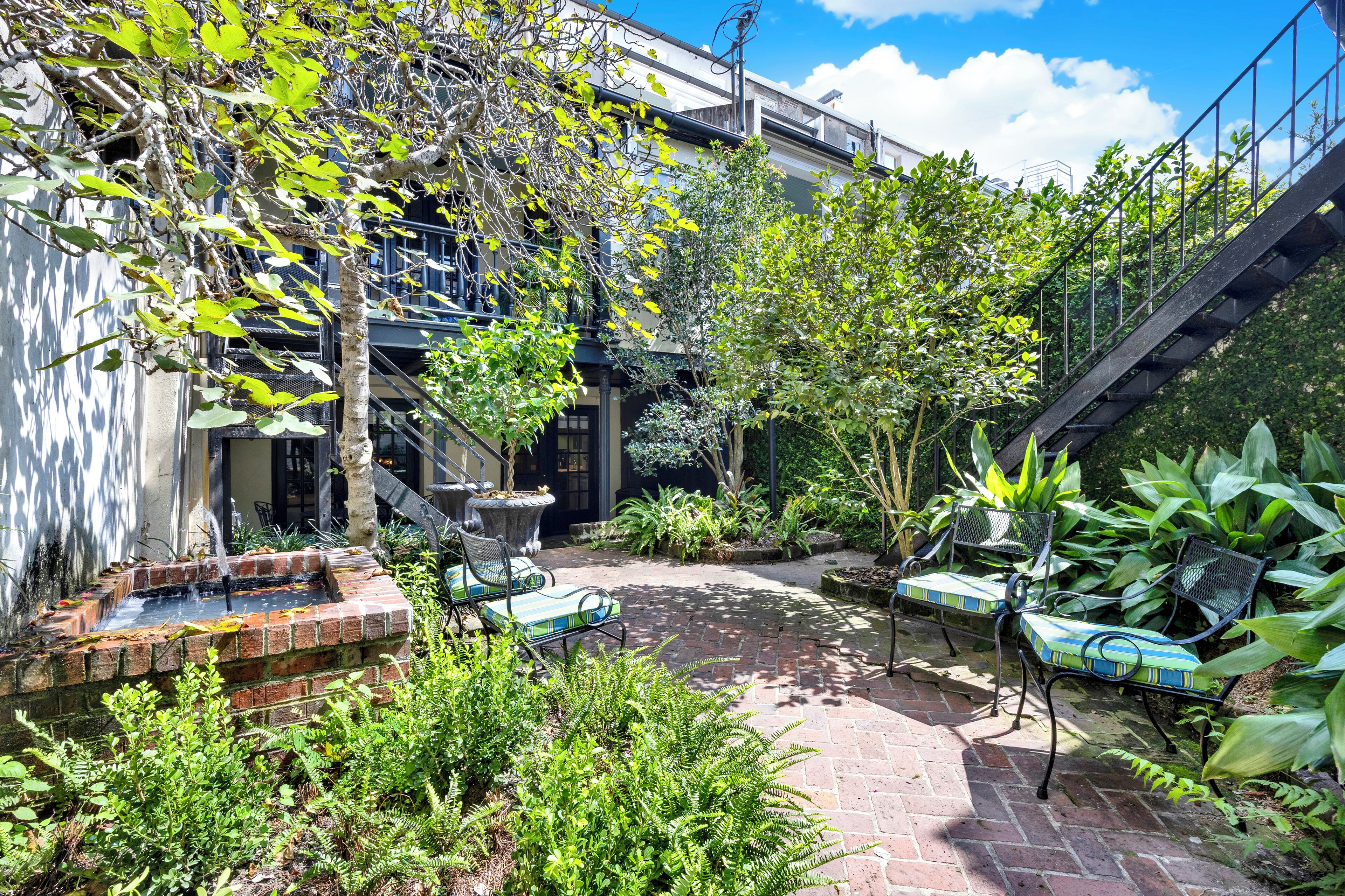 A courtyard with a brick fountain, lounge chairs, and lush greenery.