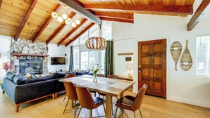 A modern living room with a wooden ceiling, stone fireplace, and a dining area with a wooden table and chairs. - Game Room + Deck: Wooded Big Bear Lake Retreat (Big Bear Lake)