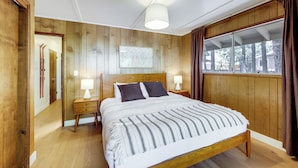 A wooden-paneled bedroom with a large bed, two bedside tables, a ceiling light, and a window with curtains. - Game Room + Deck: Wooded Big Bear Lake Retreat (Big Bear Lake)