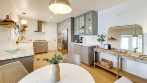 A modern kitchen with a central island, wooden cabinets, and a dining area with a white table and chairs. - Game Room + Deck: Wooded Big Bear Lake Retreat (Big Bear Lake)