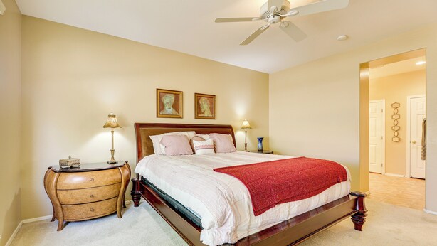 A bedroom with a wooden bed, two bedside tables, a nightstand, a ceiling fan, and a door leading to another room. - Pool Access: Oakwood Home in Sun Lakes (Chandler)