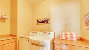 A laundry area with a white washer and dryer, wooden cabinets, a 'Laundry' sign, and a checkered towel on the counter. - Pool Access: Oakwood Home in Sun Lakes (Chandler)