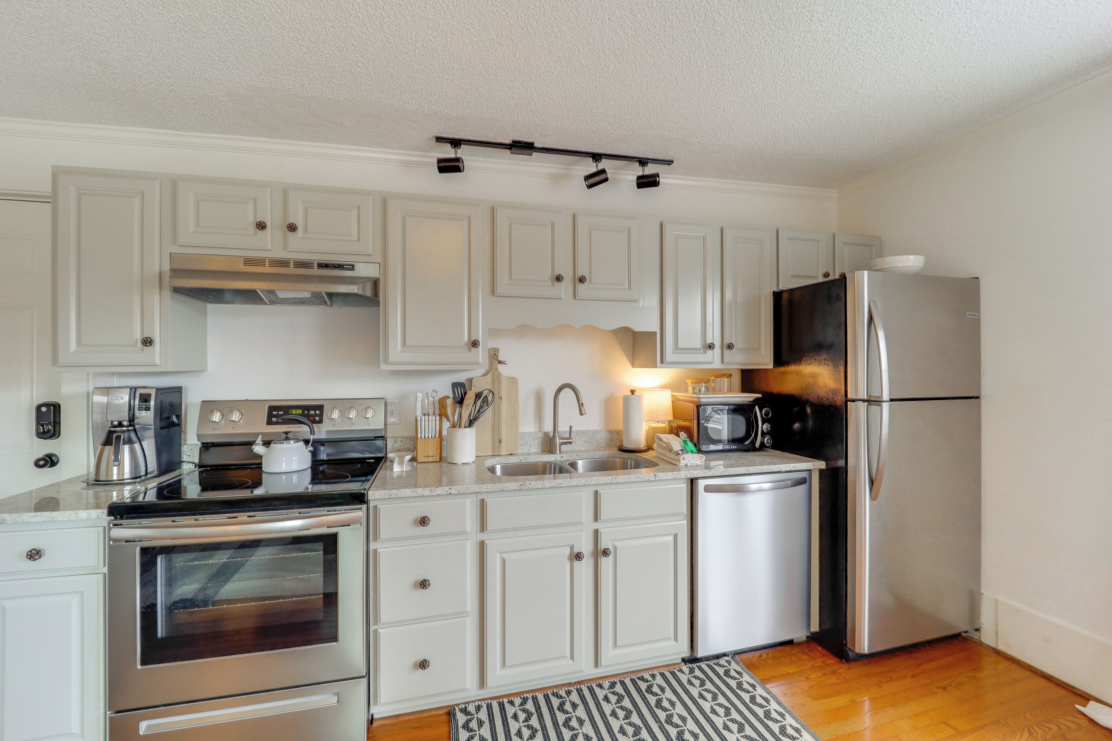 A modern kitchen with white cabinets, stainless steel appliances, and a patterned rug.
