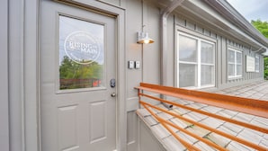 A building with a grey facade, a door with a window, and a metal railing. - Shop, Dine & Unwind: Dtwn Blowing Rock Retreat! (Blowing Rock)