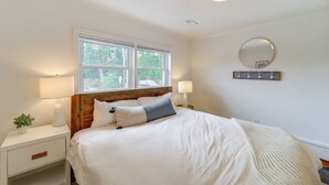 A bedroom with a large bed, two bedside lamps, a round mirror, and a window with a view of greenery. - Shop, Dine & Unwind: Dtwn Blowing Rock Retreat! (Blowing Rock)