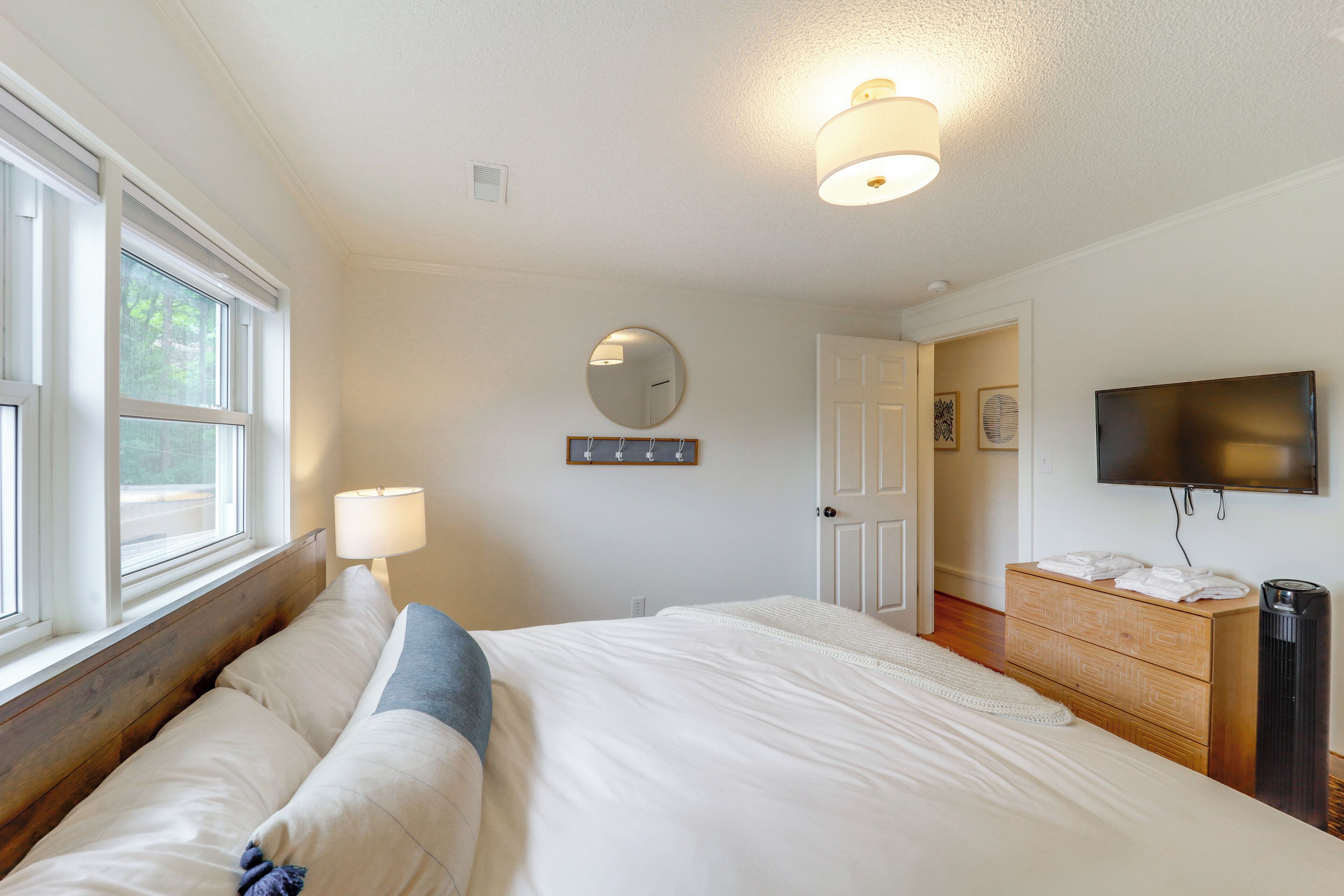 A bedroom with a bed, bedside lamp, dresser, TV, and a mirror on the wall.