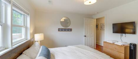 A bedroom with a bed, bedside lamp, dresser, TV, and a mirror on the wall.
