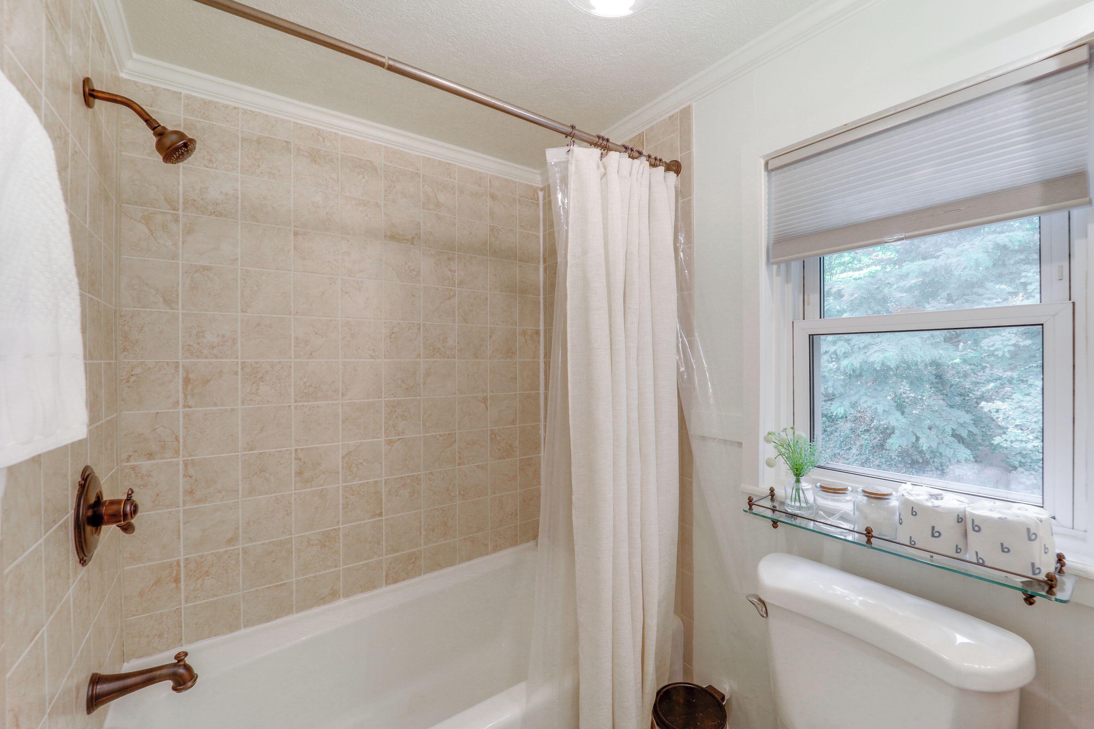 A bathroom with a bathtub, a toilet, and a window with a view of trees.
