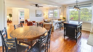 Un salón amplio con una mesa de comedor de madera, asientos cómodos, una chimenea y ventanas grandes que ofrecen vistas a zonas verdes.